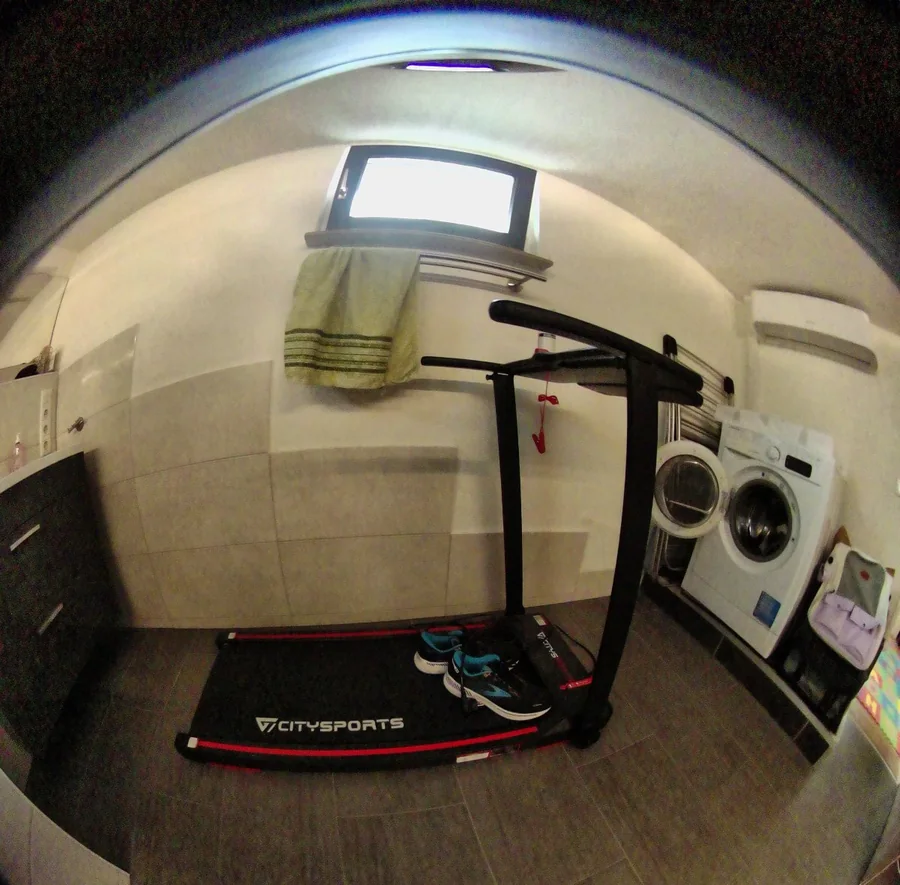 A raw fisheye camera frame from the scanner showing a small room with a treadmill, a washing machine and a window